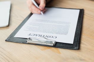 partial view of businessman signing contract on clipboard