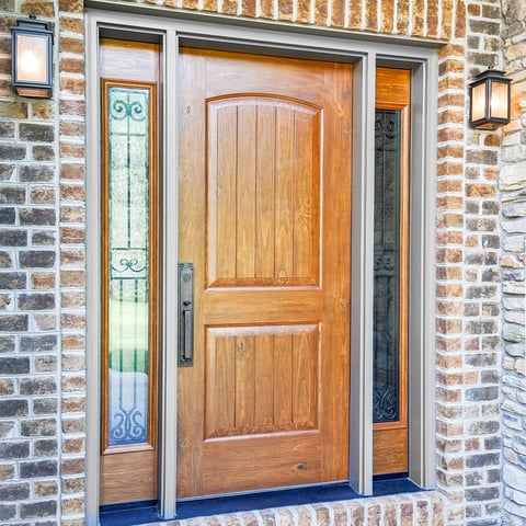 Stained woodgrain fiberglass entry door with two decorative glass sidelights on a brick home