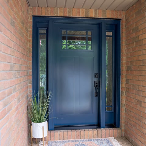 Navy blue painted steel entry door with glass and sidelights on a brick home