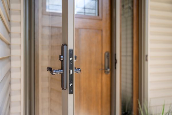 Close-up of a storm door handle in front of a wood entry door