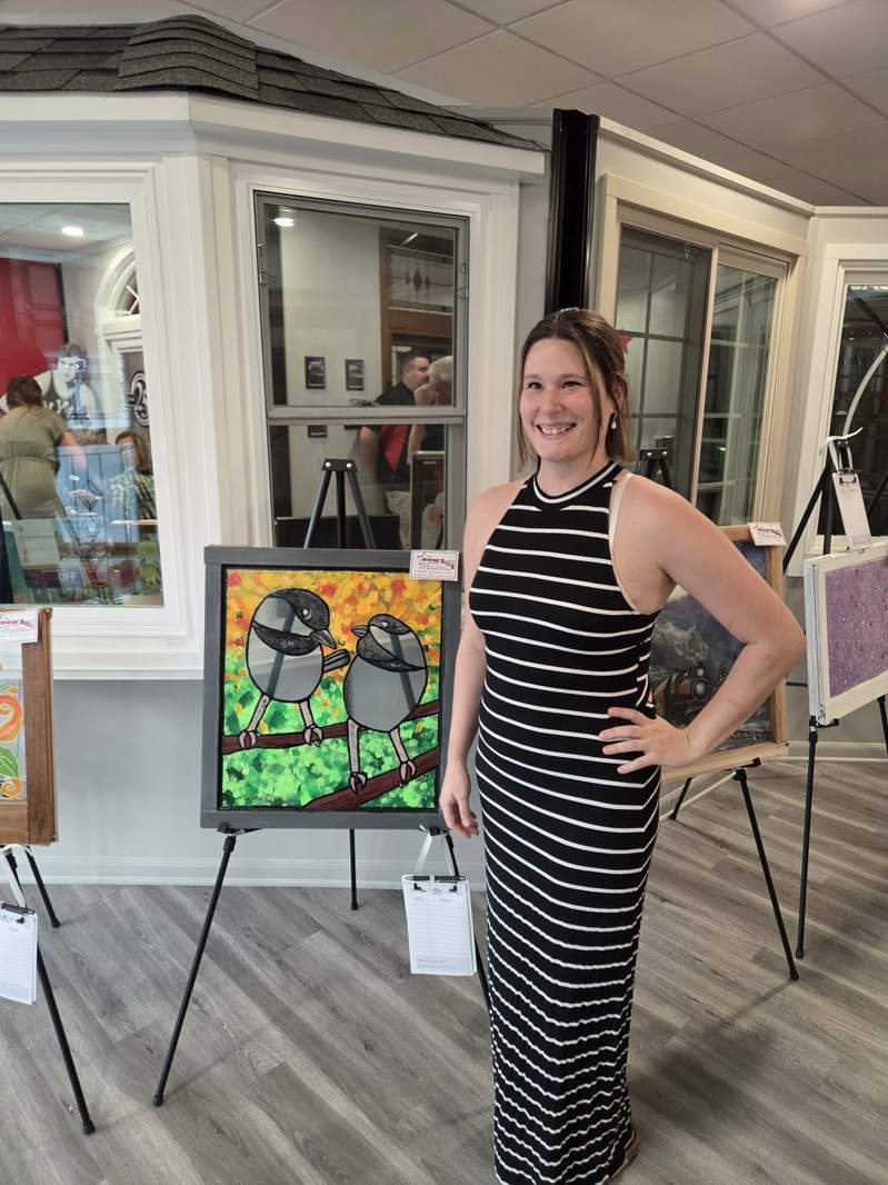 Community member in a striped dress with two colorful birds painted on a window sash at the October 1 event